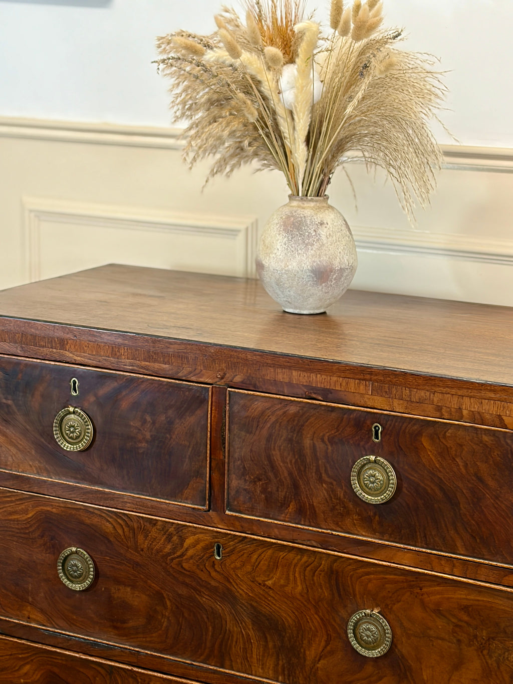 Wooden dresser with decorative vase containing dried plants on a white wall background