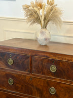 Wooden dresser with decorative vase containing dried plants on a white wall background