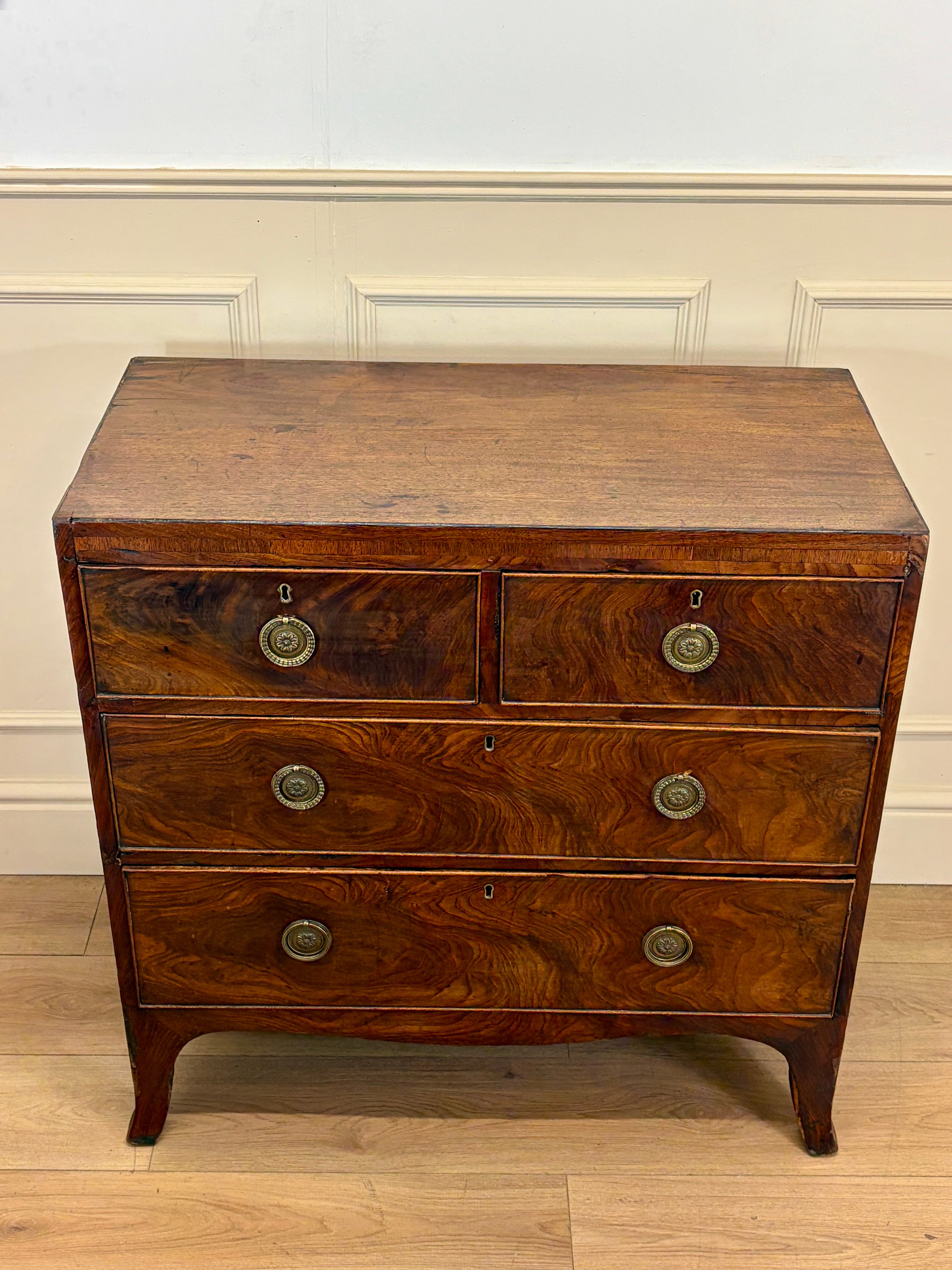 Wooden dresser with three drawers and brass handles against a white wall.
