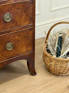 Wooden dresser with brass handles next to a wicker basket on a wooden floor.
