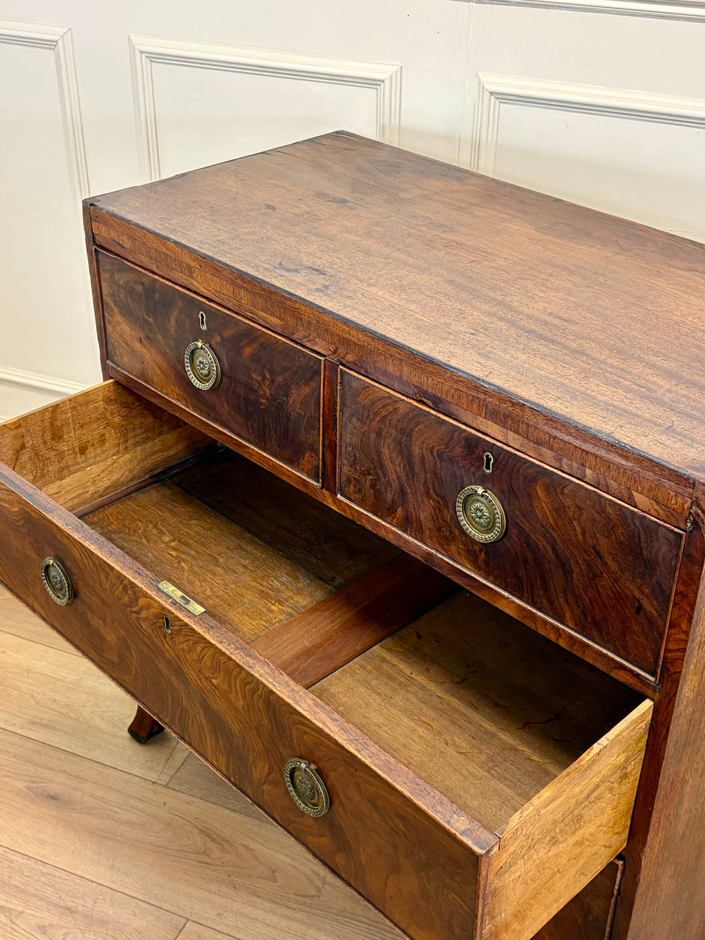 Wooden sideboard with open drawer against a white paneled wall.