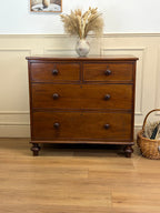 Wooden dresser with three drawers on a wooden floor, with a vase of dried plants on top.