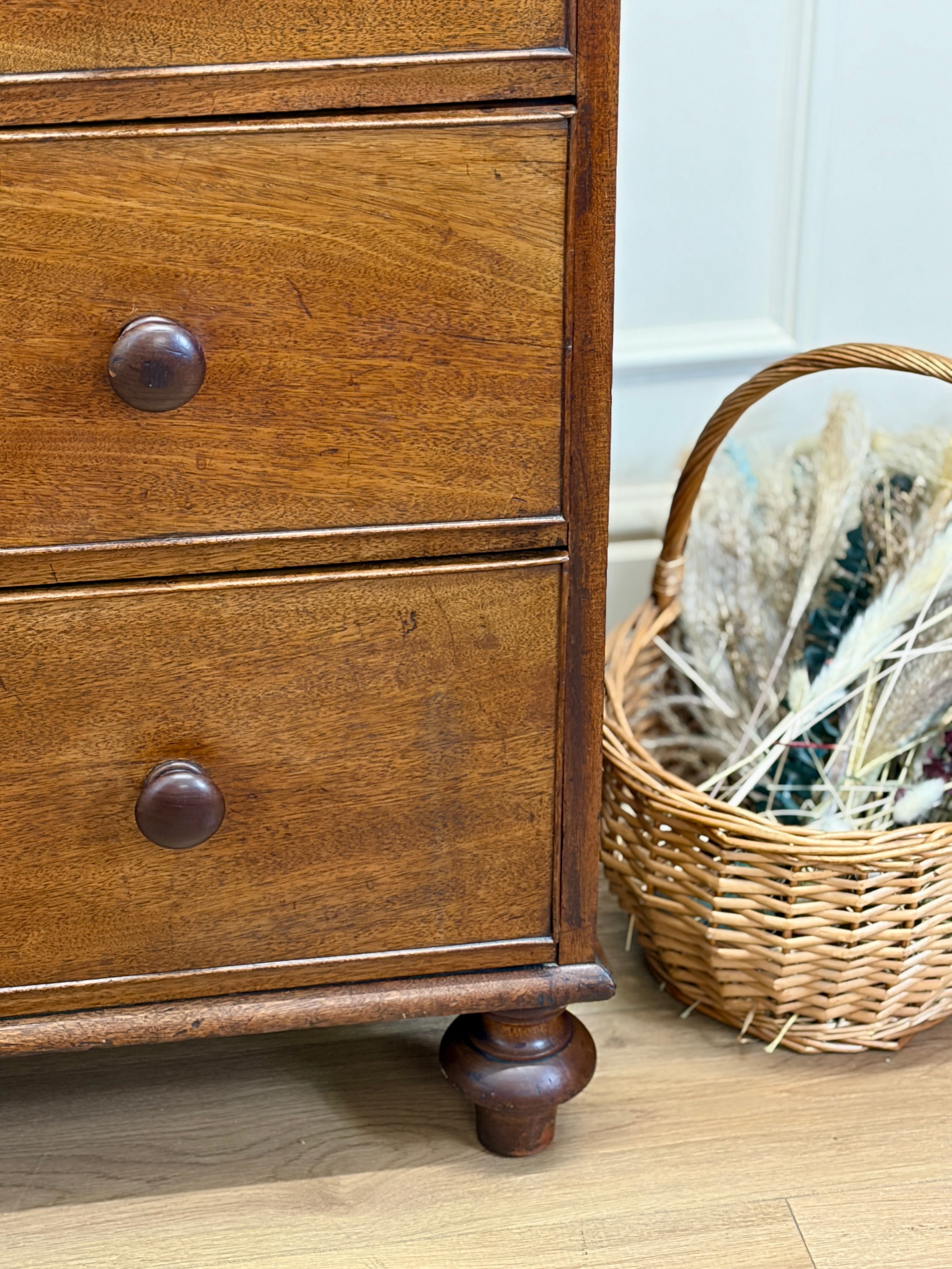 Wooden dresser with two drawers and a wicker basket on a wooden floor.