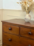 Wooden dresser with a vase of dried plants on top against a neutral wall.