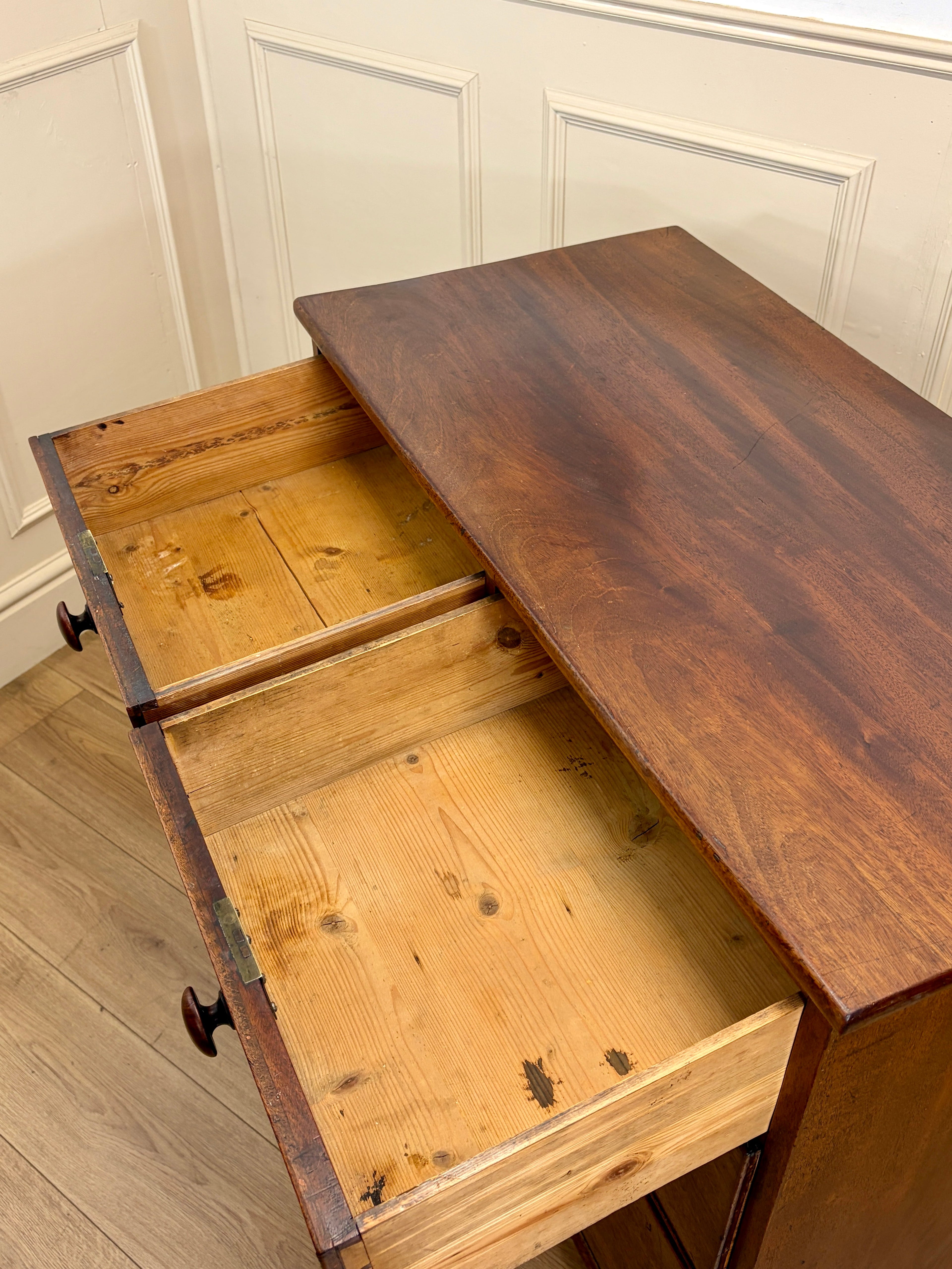 Wooden desk with an open drawer against a white paneled wall.