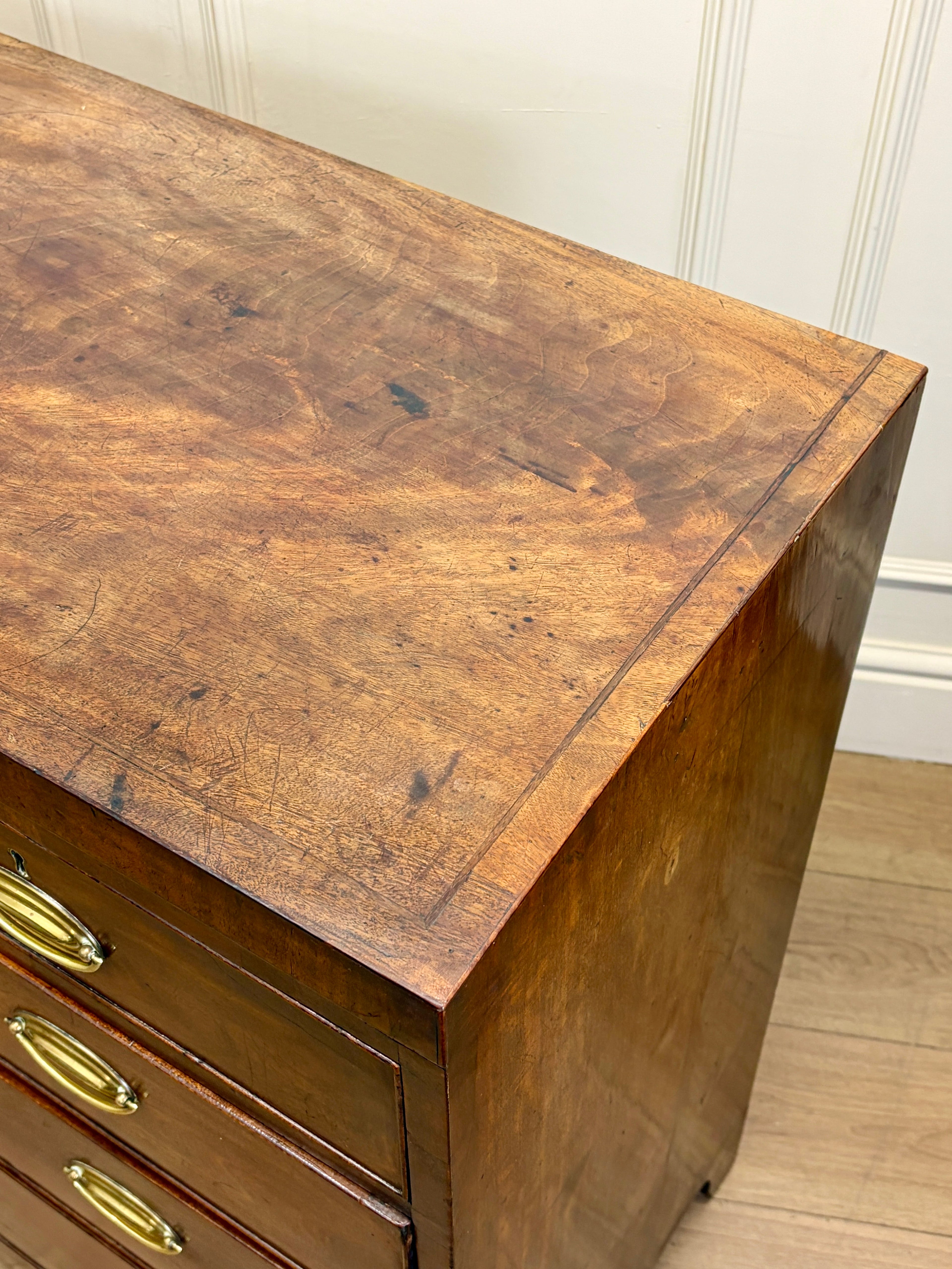 Wooden dresser with a worn surface and brass handles against a white wall.