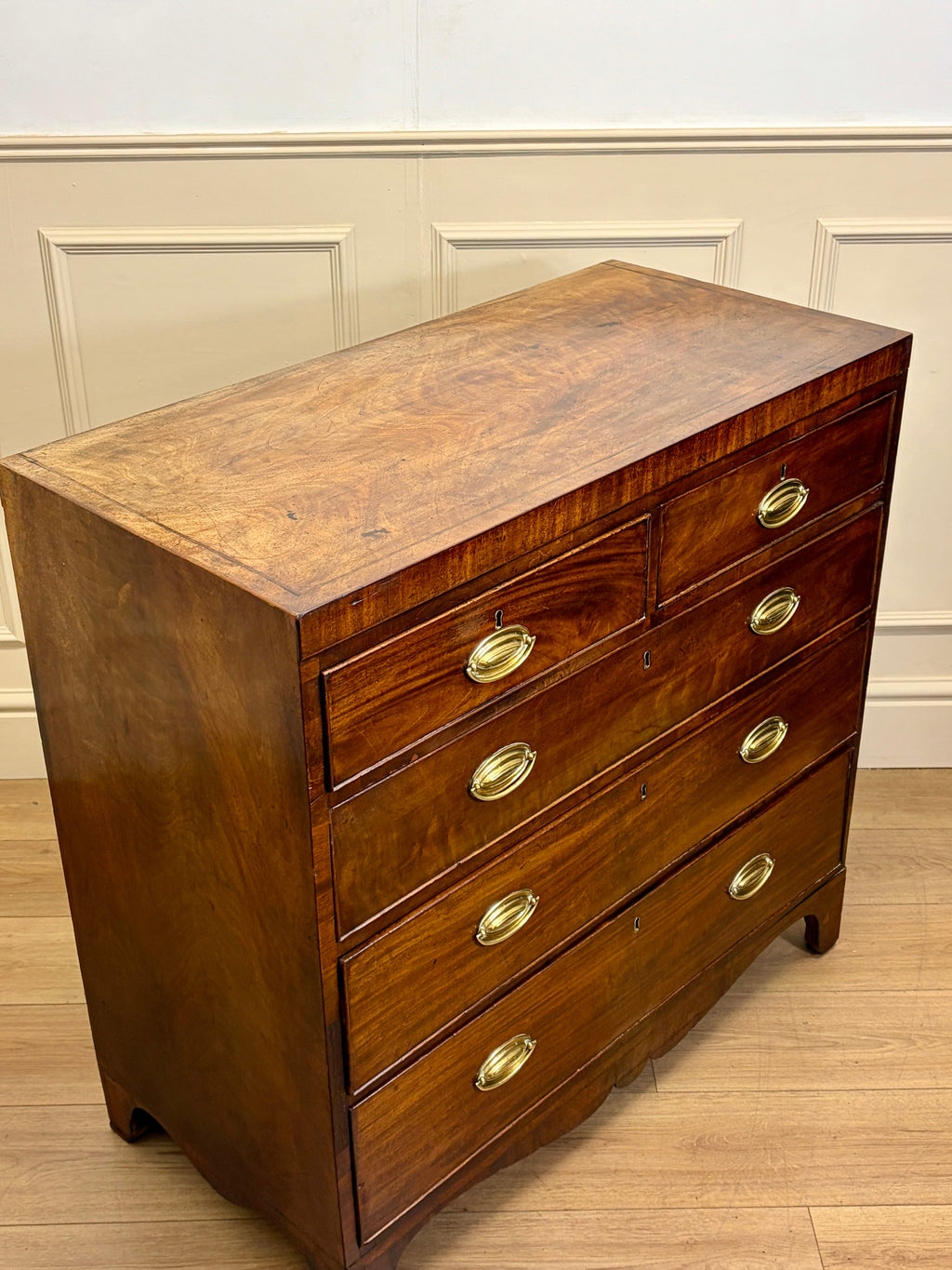 Wooden dresser with gold handles on a wooden floor against a white wall.