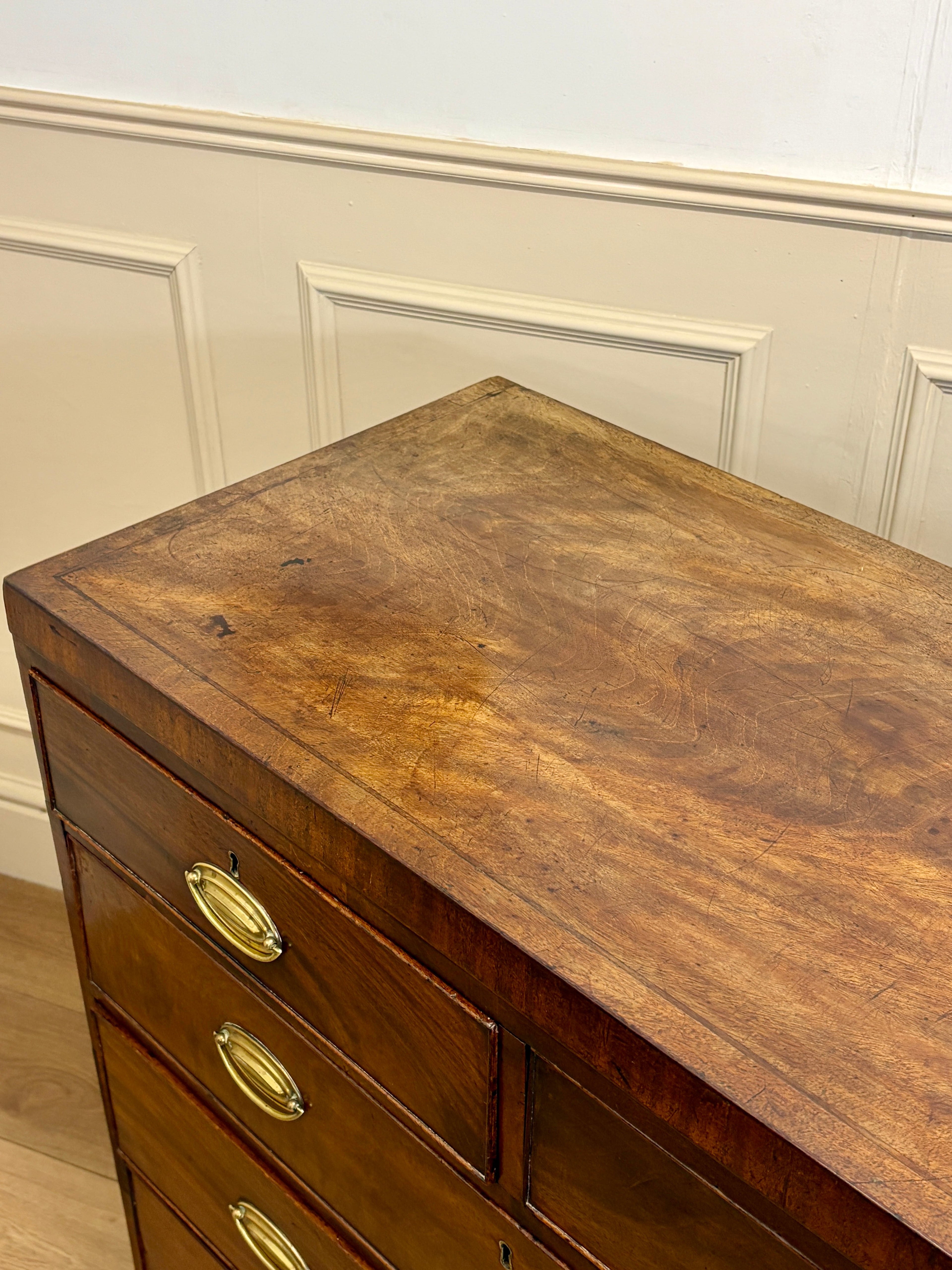 Wooden dresser with brass handles against a white paneled wall.