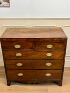 Wooden dresser with brass handles on a wooden floor.