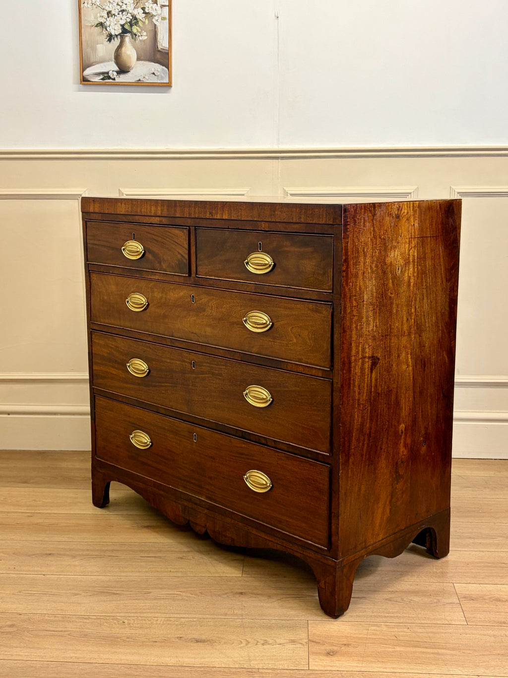 Wooden dresser with gold handles in a room with a painting on the wall.