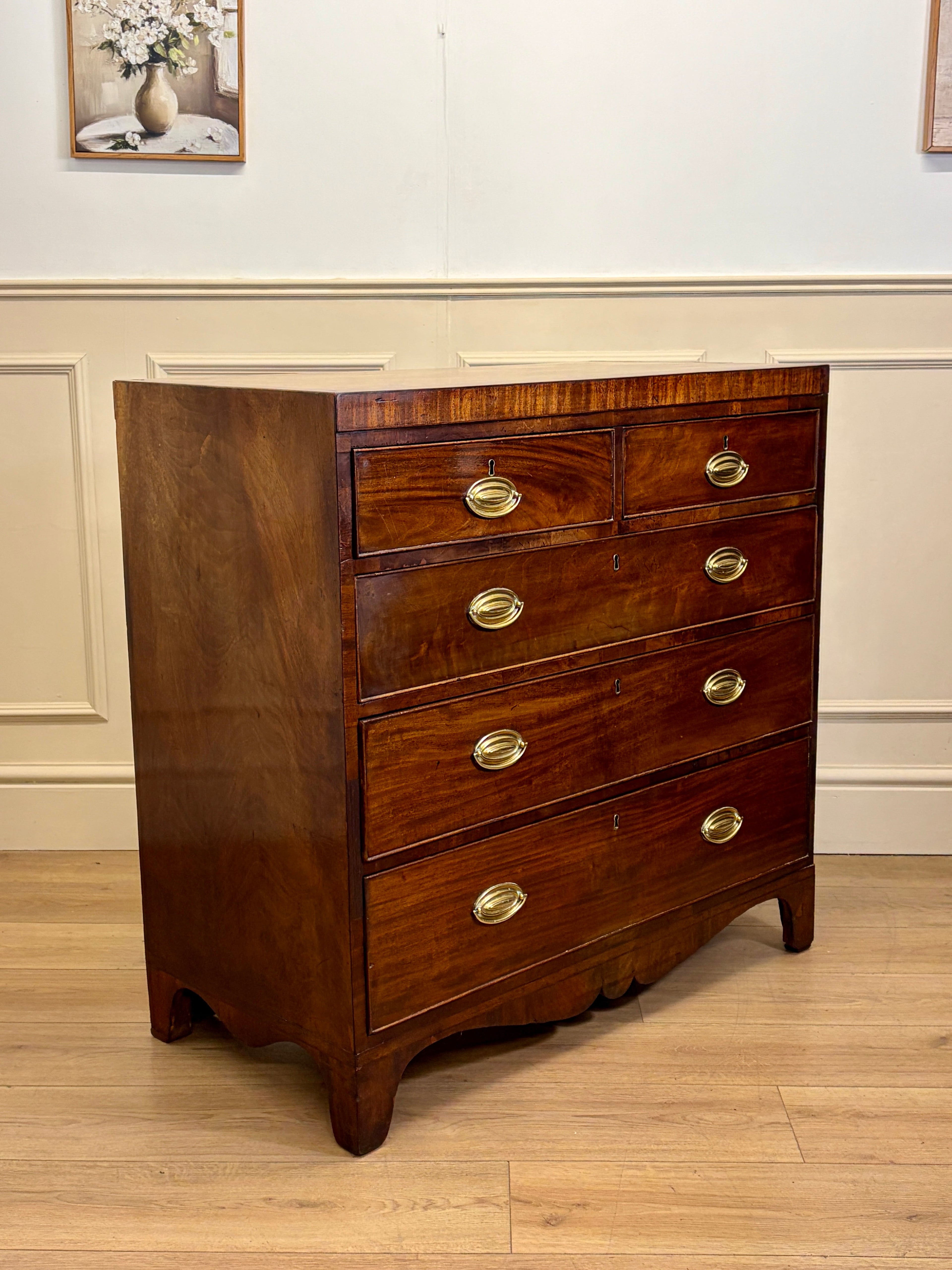 Wooden dresser with gold handles on a wooden floor against a white wall.