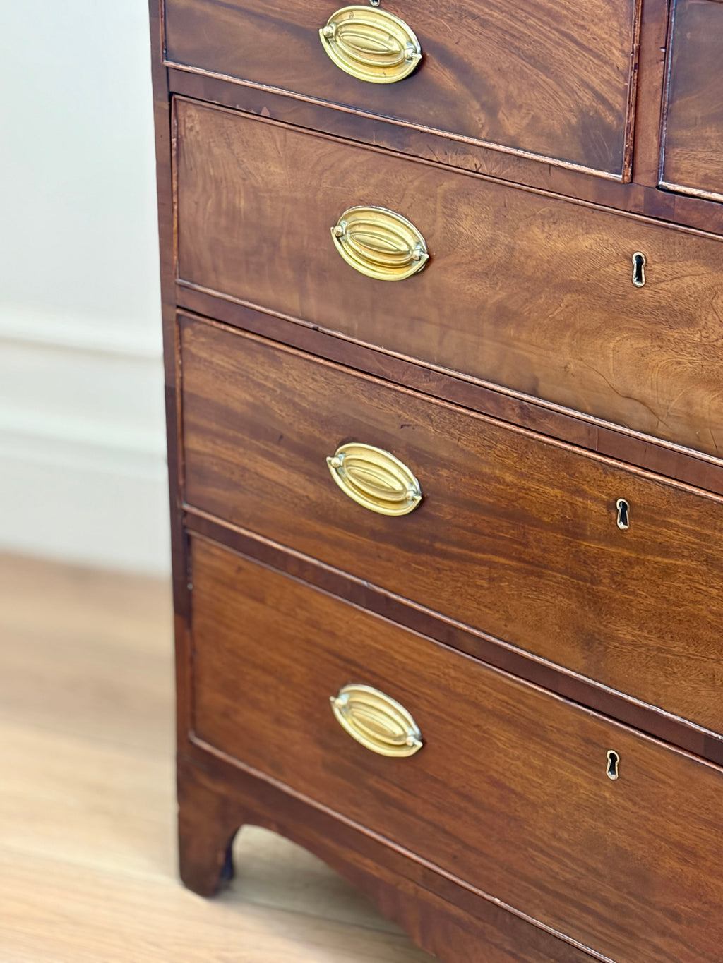 Wooden dresser with brass handles on a light wooden floor.