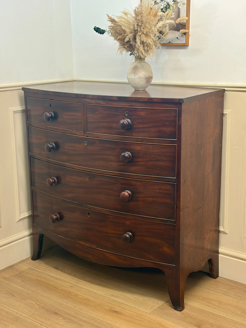 Wooden dresser with four drawers in a room with light-colored walls and wooden floor.