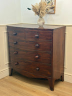 Wooden dresser with four drawers in a room with light-colored walls and wooden floor.