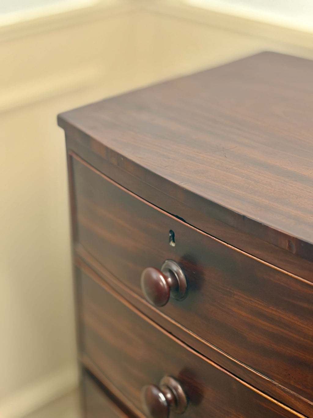 Wooden dresser with two drawers and metal handles against a beige wall.