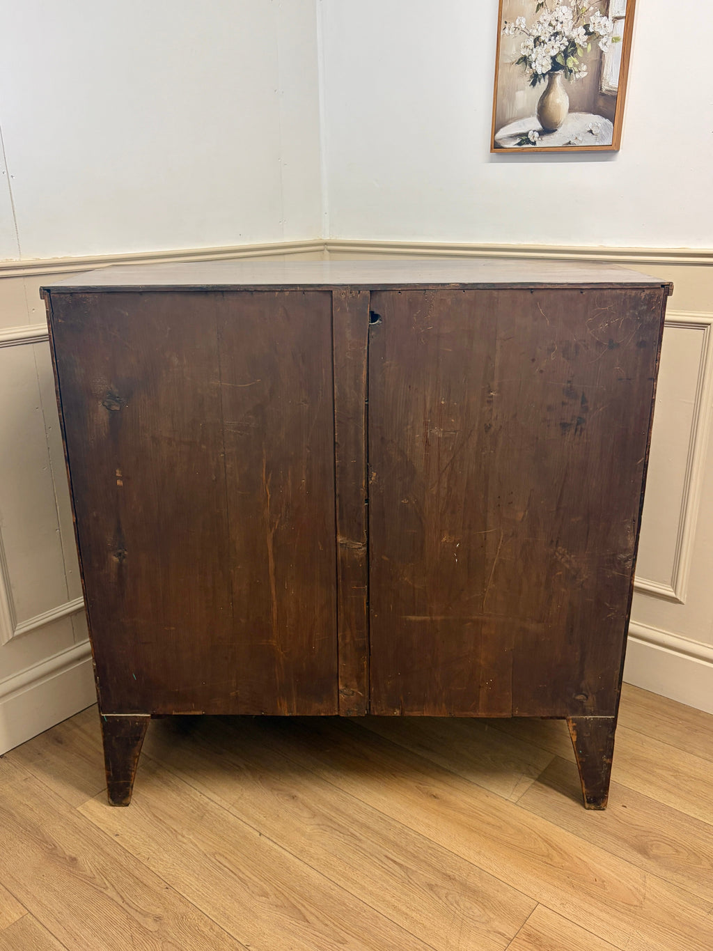 Wooden cabinet with a floral painting on the wall in the background