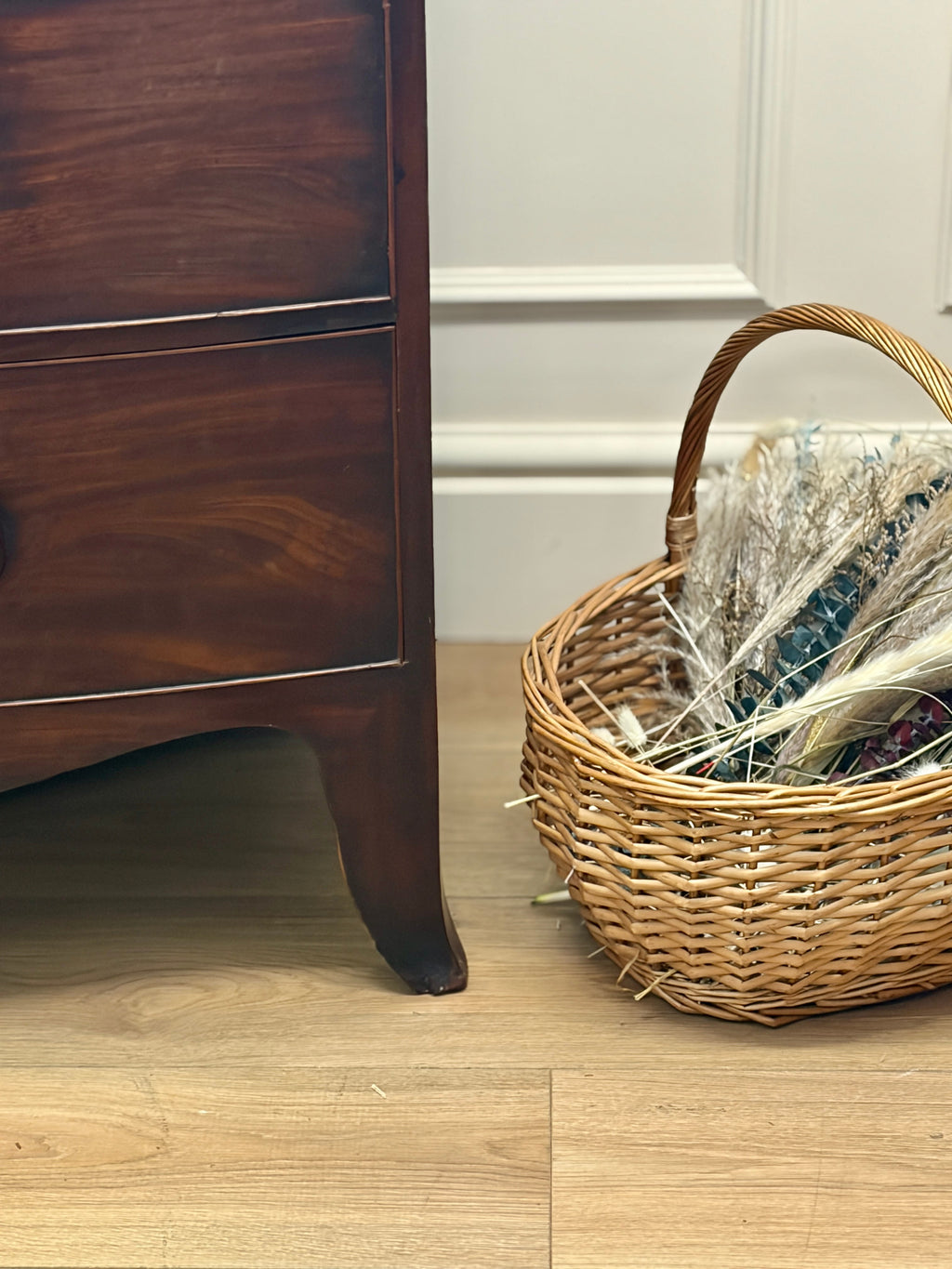 Wicker basket with decorative items next to a wooden cabinet on a wooden floor.