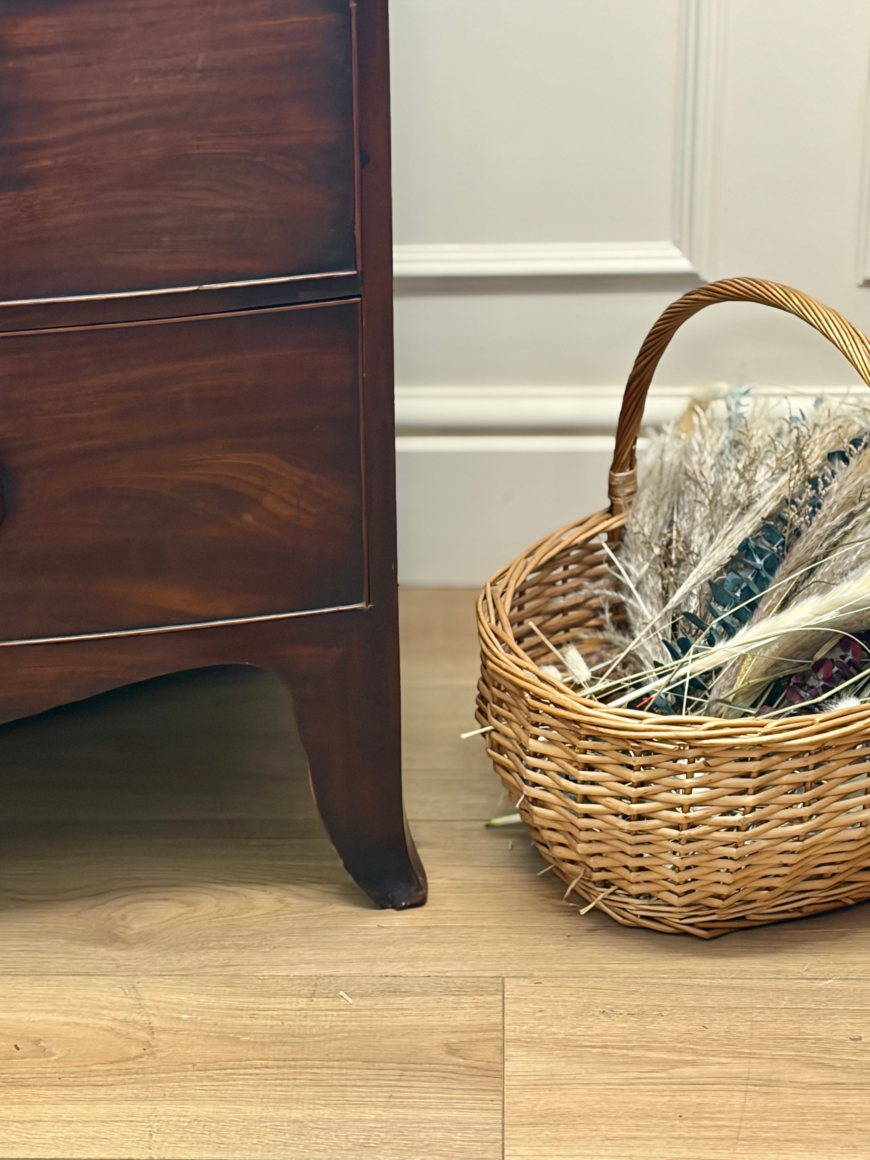 Wicker basket with decorative items next to a wooden cabinet on a wooden floor.