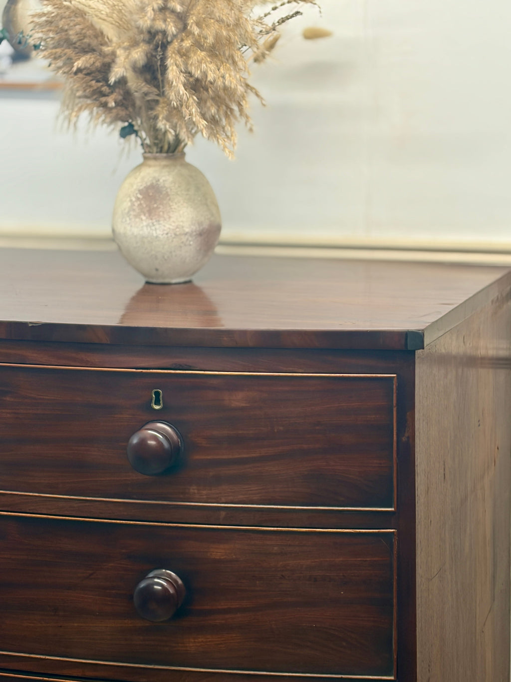 Wooden dresser with a vase of dried plants on top