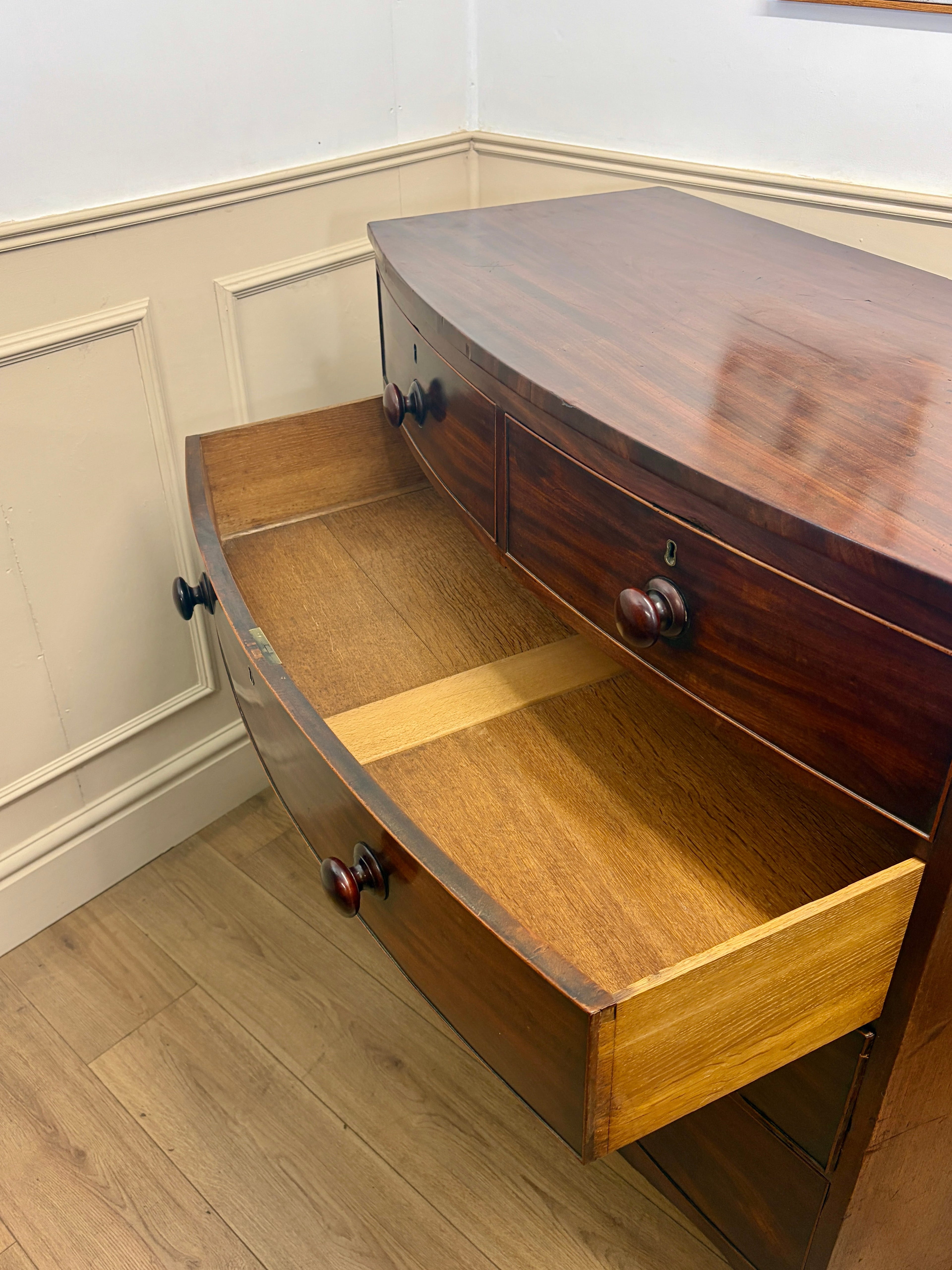 Wooden desk with a drawer open on a wooden floor against a white wall.