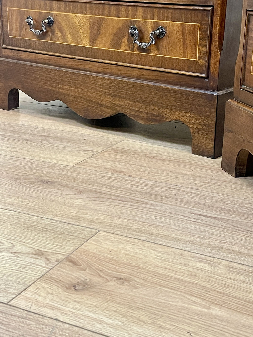 Vintage pair of mahogany bedside chest of drawers with five drawers each, featuring decorative inlaid tops and brass handles, displayed against a cream wall on a wooden floor.