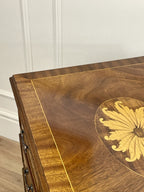 Vintage pair of mahogany bedside chest of drawers with five drawers each, featuring decorative inlaid tops and brass handles, displayed against a cream wall on a wooden floor.