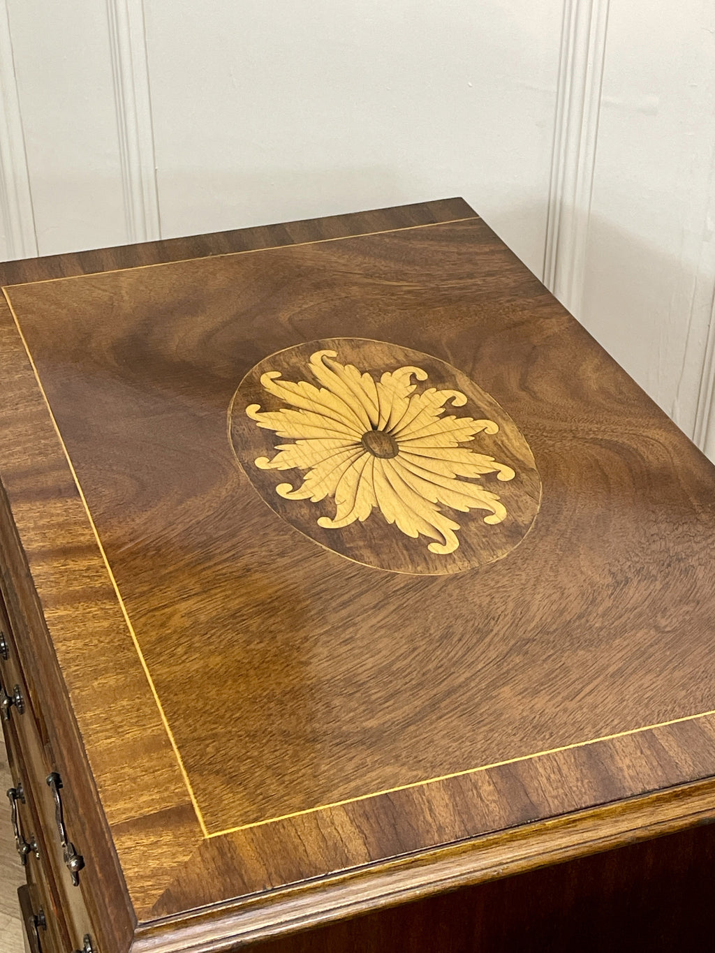 Wooden chest with a decorative gold inlay design on a white paneled wall background