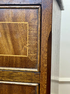 Vintage pair of mahogany bedside chest of drawers with five drawers each, featuring decorative inlaid tops and brass handles, displayed against a cream wall on a wooden floor.