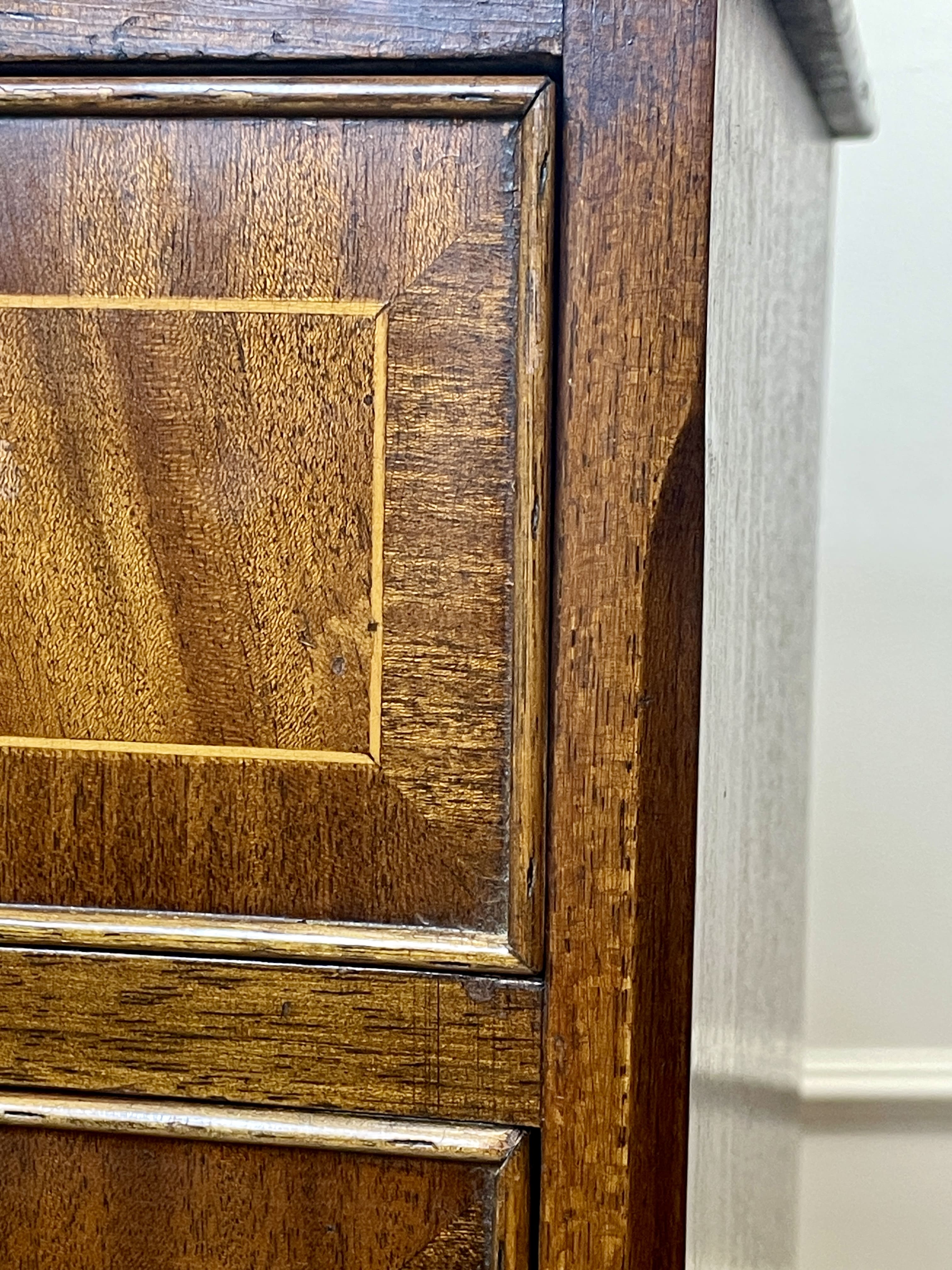 Vintage pair of mahogany bedside chest of drawers with five drawers each, featuring decorative inlaid tops and brass handles, displayed against a cream wall on a wooden floor.