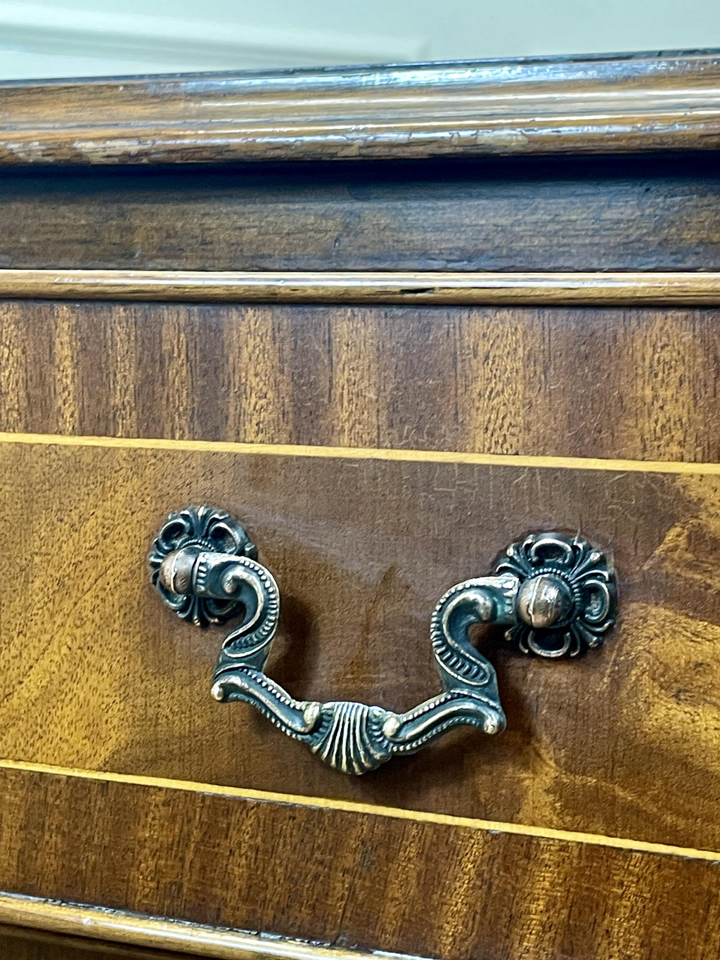 Vintage pair of mahogany bedside chest of drawers with five drawers each, featuring decorative inlaid tops and brass handles, displayed against a cream wall on a wooden floor.