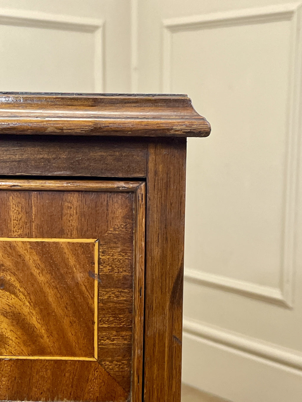Vintage pair of mahogany bedside chest of drawers with five drawers each, featuring decorative inlaid tops and brass handles, displayed against a cream wall on a wooden floor.