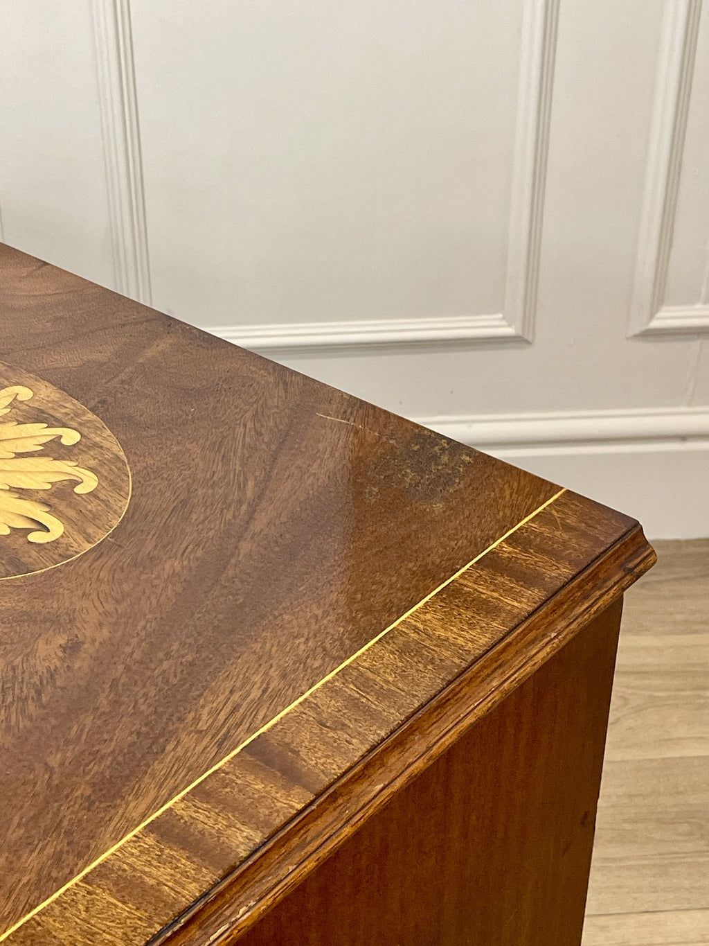 Vintage pair of mahogany bedside chest of drawers with five drawers each, featuring decorative inlaid tops and brass handles, displayed against a cream wall on a wooden floor.