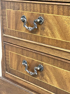 Vintage pair of mahogany bedside chest of drawers with five drawers each, featuring decorative inlaid tops and brass handles, displayed against a cream wall on a wooden floor.