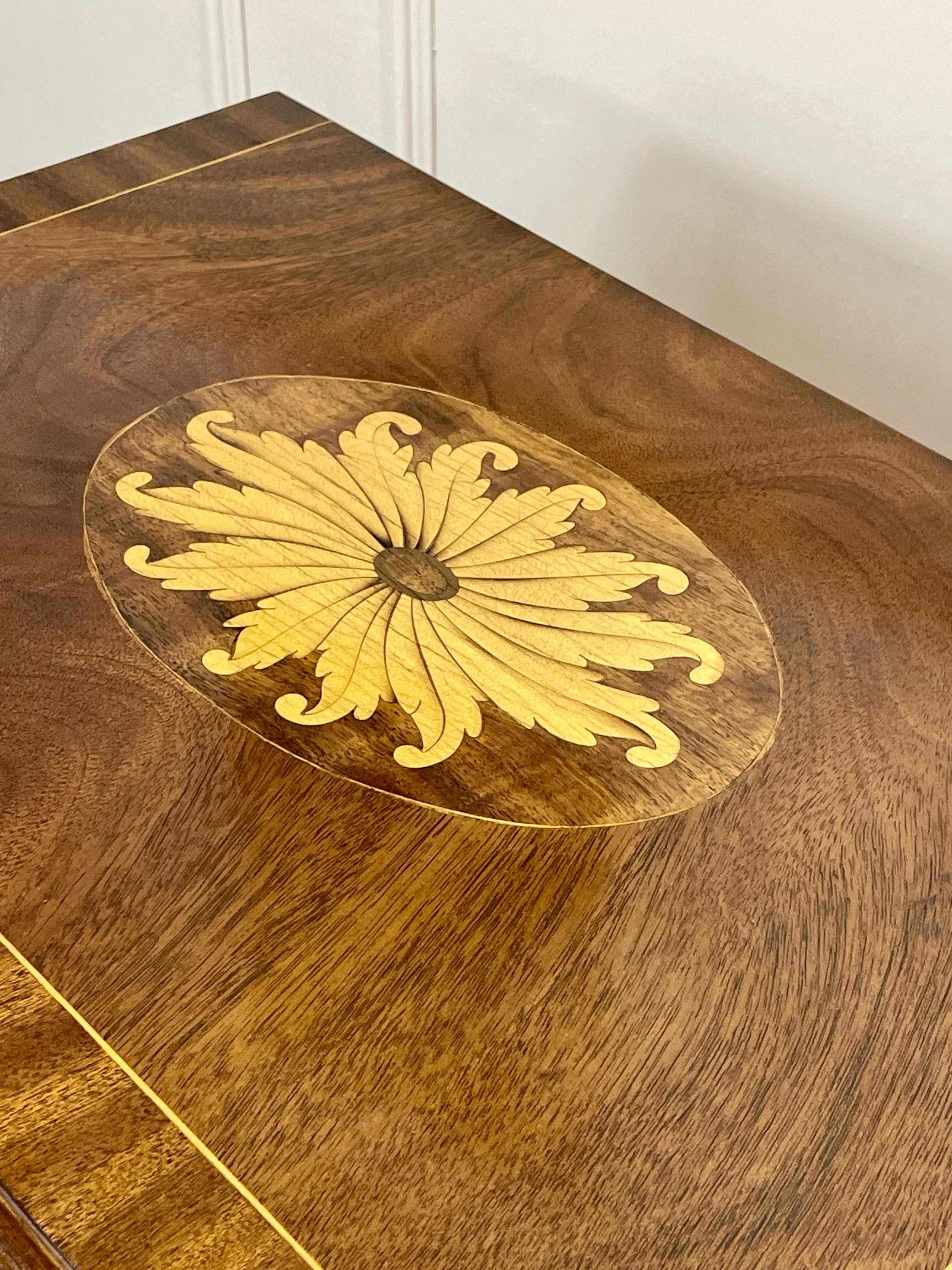 Vintage pair of mahogany bedside chest of drawers with five drawers each, featuring decorative inlaid tops and brass handles, displayed against a cream wall on a wooden floor.