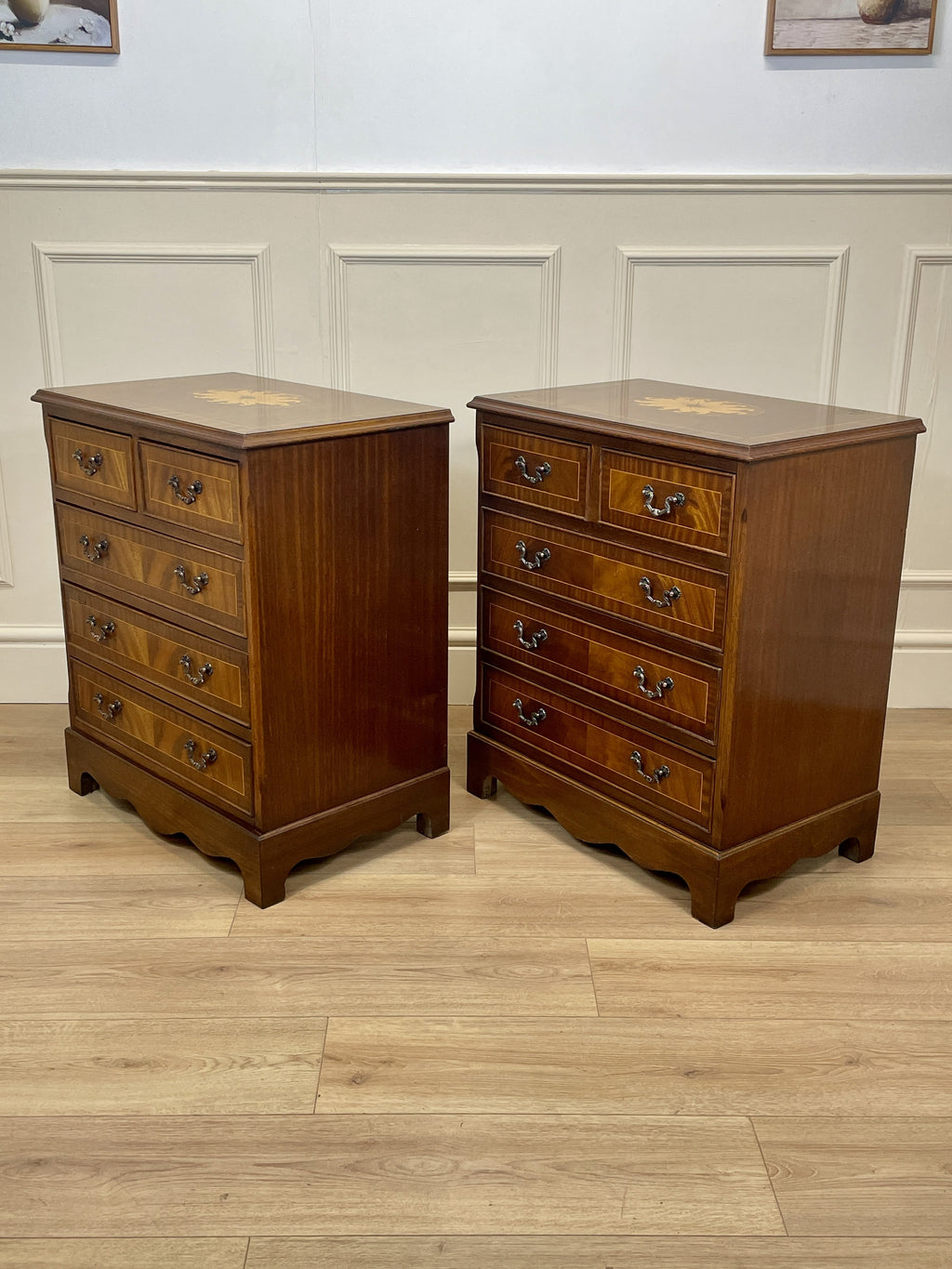 Two wooden dressers with inlaid designs on a wooden floor against a white paneled wall.