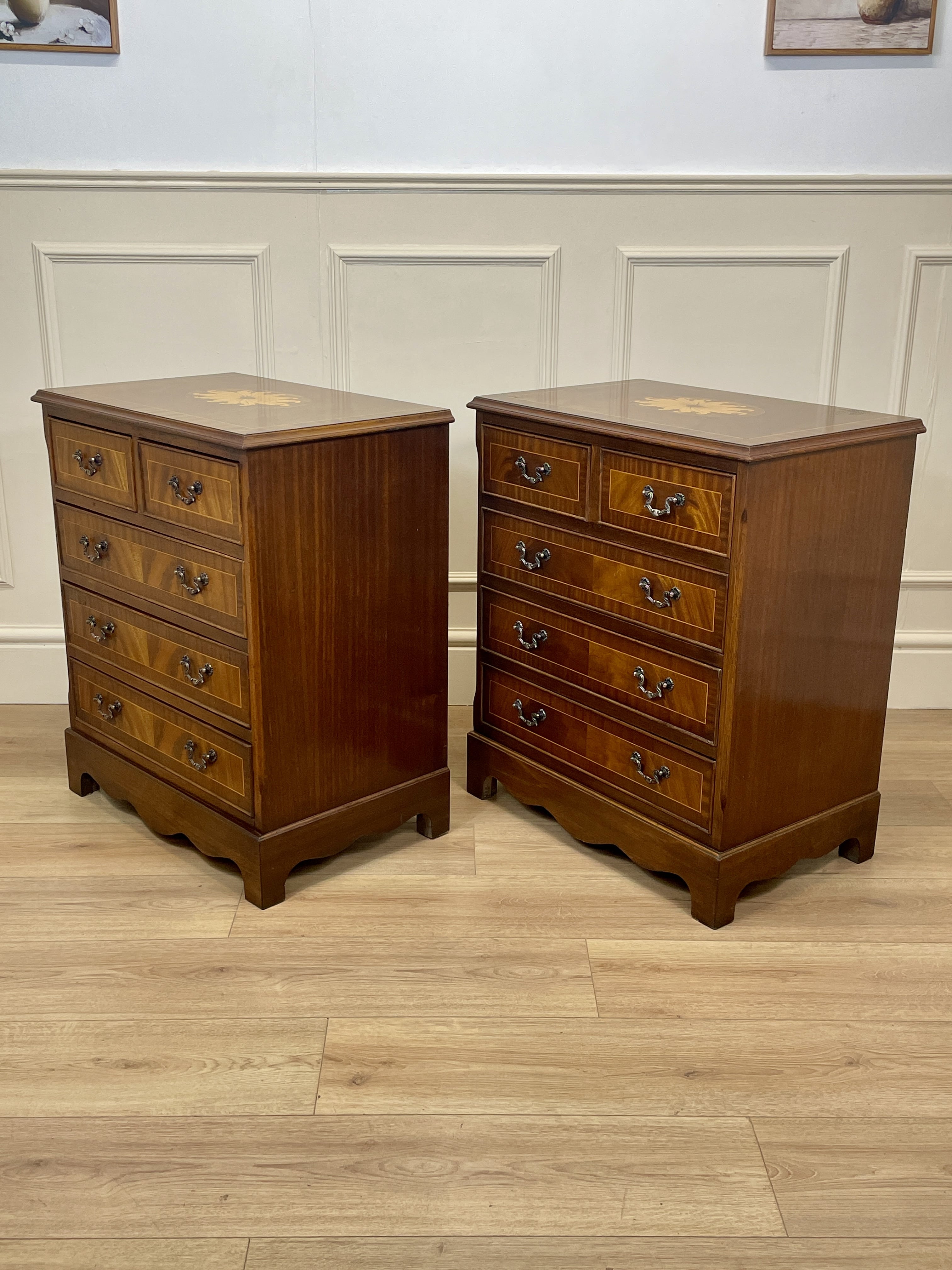 Two wooden dressers with inlaid designs on a wooden floor against a white paneled wall.