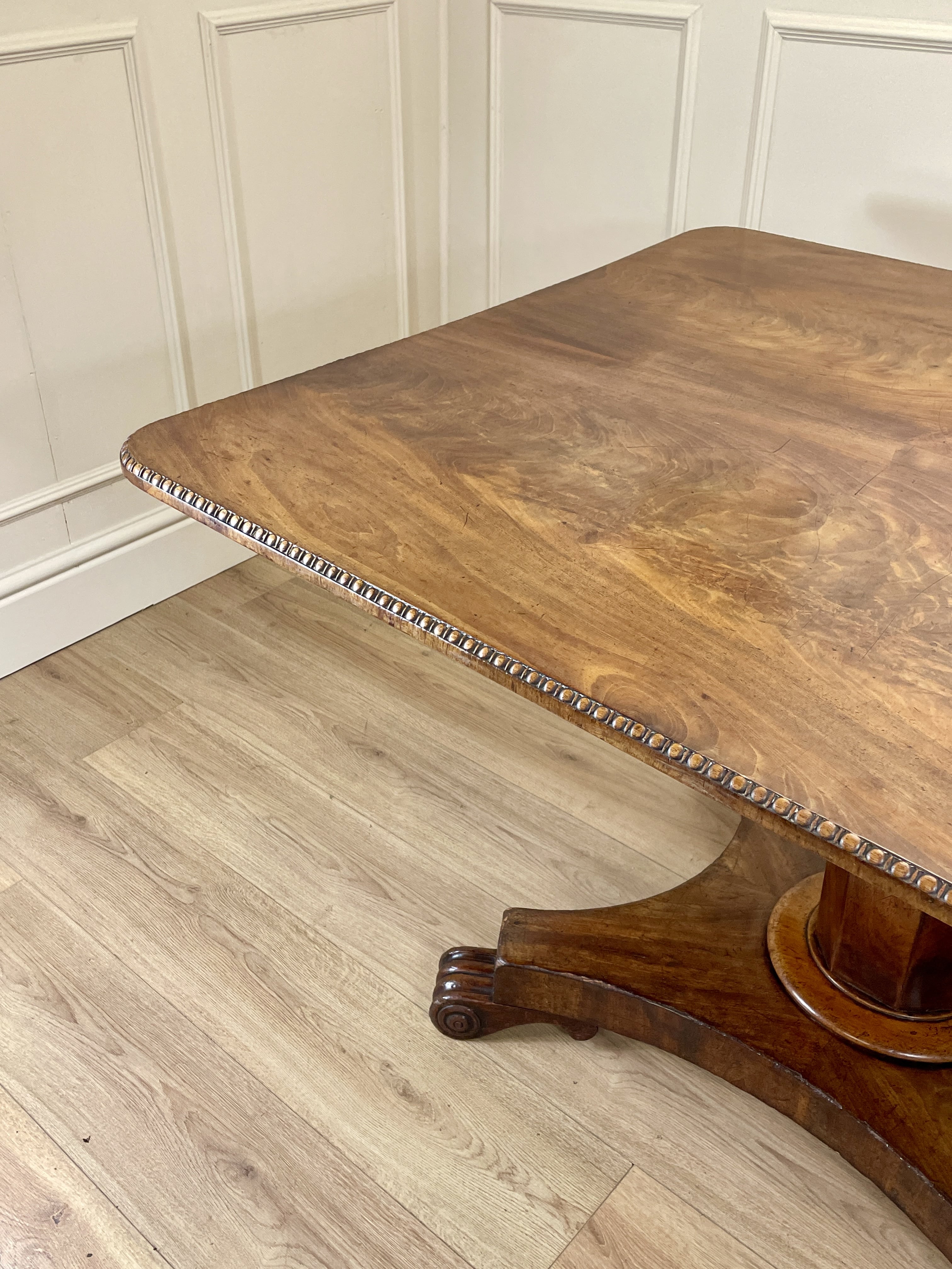 Wooden table with a decorative edge on a wooden floor against a white paneled wall.