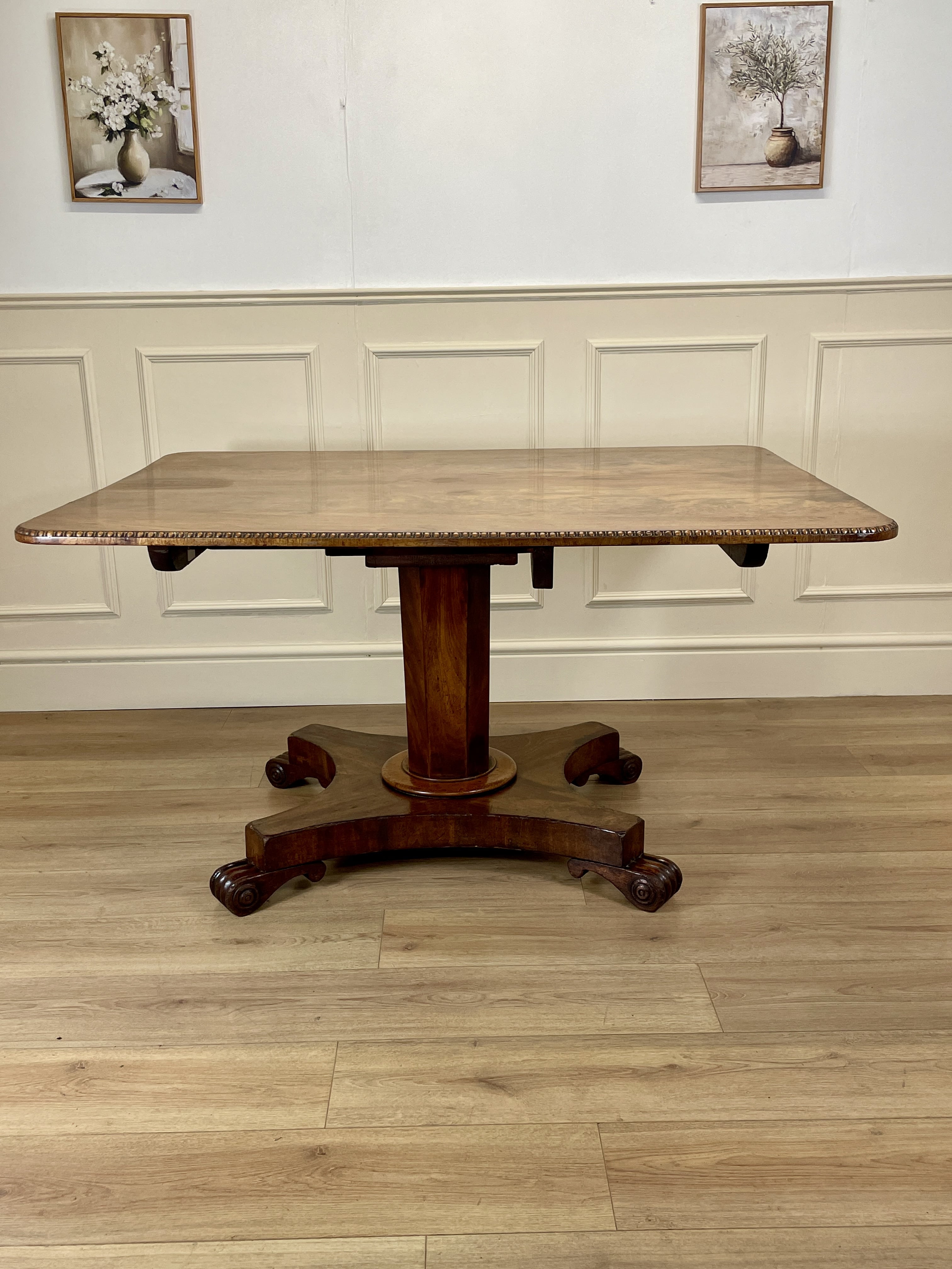 Wooden pedestal table in a room with white paneled walls and wooden flooring.